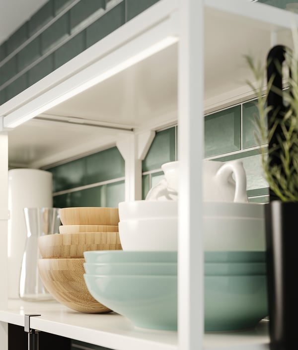Well-organized kitchen shelf with white bowls, woven baskets, vases, and a green plant in a corner.