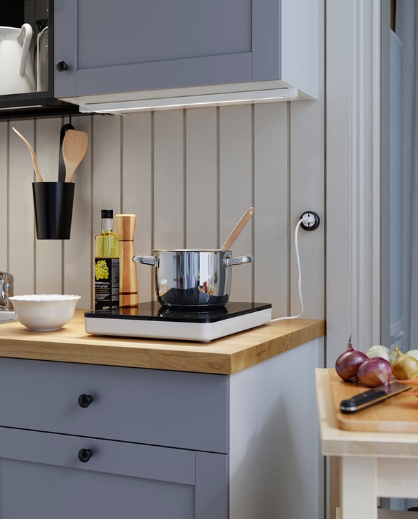 Kitchen with gray cabinets, wooden counter, onions, knife, pots, utensils.