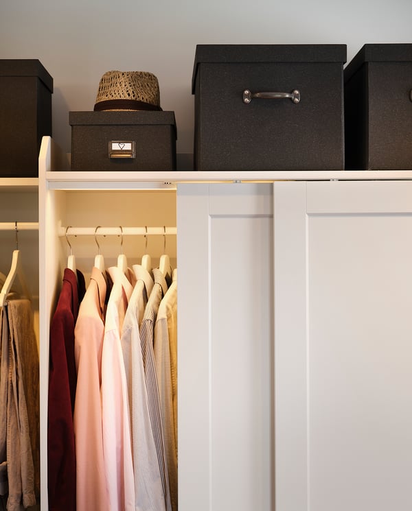 Organized closet with white hangers, colorful clothes, and black storage boxes on shelves.