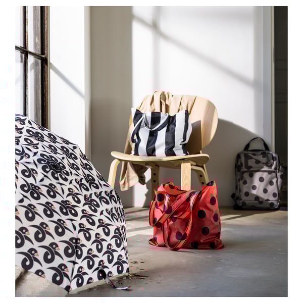 Four colorful SKYNKE bags shown indoors, two on floor, one on chair, one near windows. Lightweight, foldable, 100% recycled polyester.