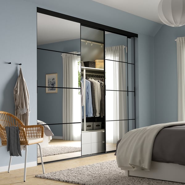 Bedroom with large, light blue closet door featuring mirrored panels. Grey bed, wicker chair, and hanging garment visible.