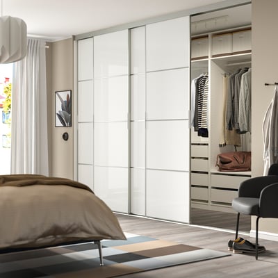 Modern bedroom with large mirrored wardrobe, neatly arranged clothes, and soft lighting.