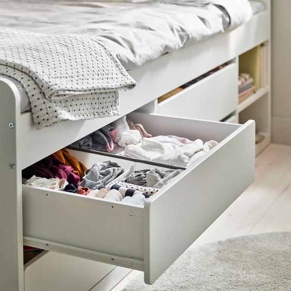 Bed with open drawer showing neatly folded clothes. Grey polka dot blanket on bed. Ladder-style steps on side.