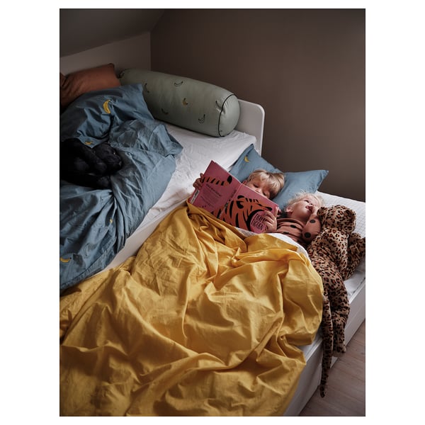 Two children reading in bed; yellow blanket, blue sheets, pillows, stuffed animals.