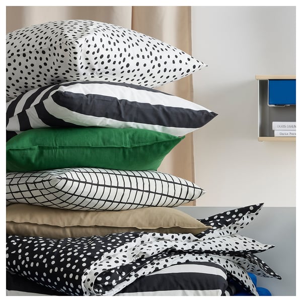 Stack of colourful pillows: black-white stripes, green, black-white grid, beige, black-white dots on bed.
