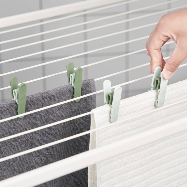 Hand hangs laundry using SLIBB pegs on drying line, shown are green and white pegs securing towels.