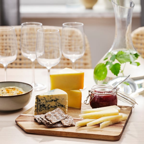 Wooden chopping board holds cheese, knife, and crackers. Four wine glasses line the back.