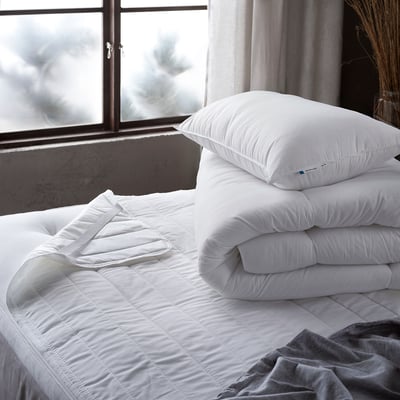 Two white pillows stacked on an unmade bed, one larger than the other.