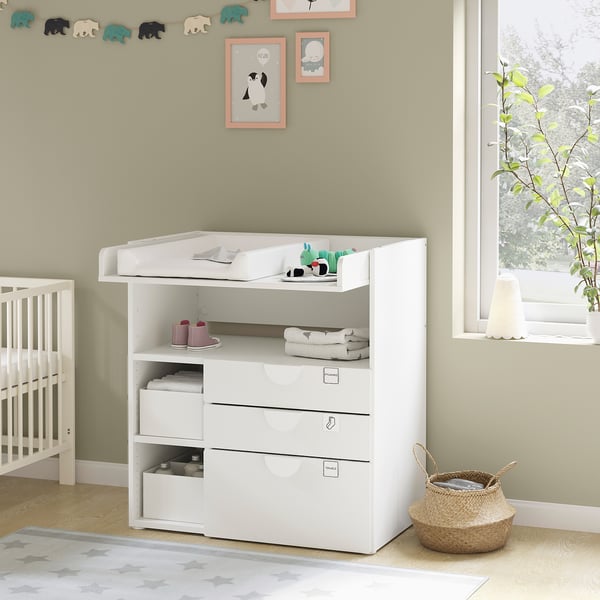 Modern white baby changing station with drawers and shelves, part of a nursery setup.
