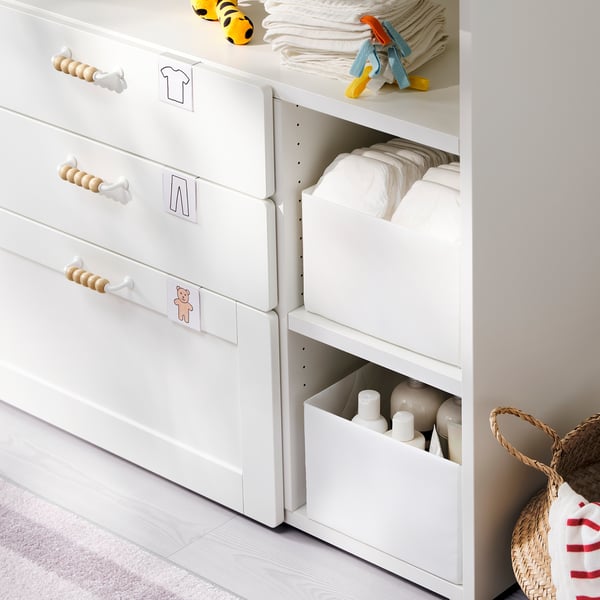 White baby changing table with storage, wooden handles, and diapers.