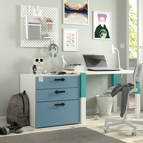 This image shows a SMÅSTAD chest of drawers in blue and white, ideal for children. It fits neatly under a desk, with wall art and a pegboard nearby.