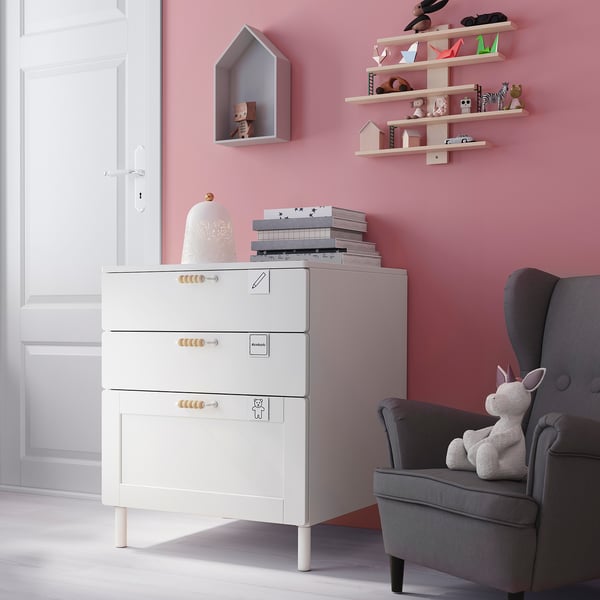 Small childs room with white storage unit, grey chair, and pink models on shelves.