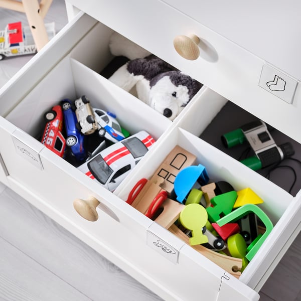 White childrens toy chest with multiple compartments filled with various toys, including cars, blocks, and stuffed animals.
