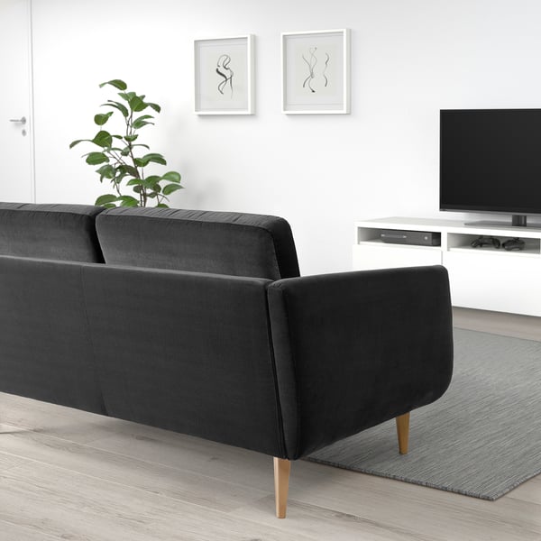 Modern living room with black velvet sofa, wooden legs, plant, wall art, tv, and grey rug.