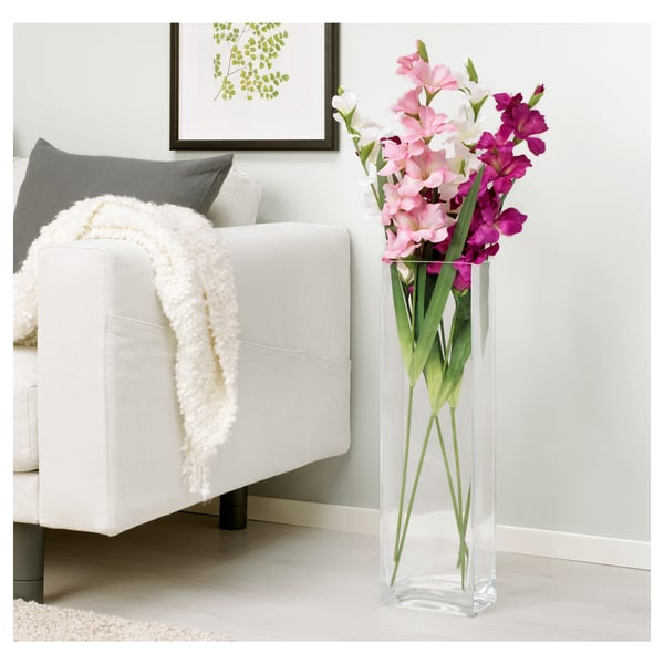 Clear vase with pink and purple flowers stands next to a white chair with a throw blanket.