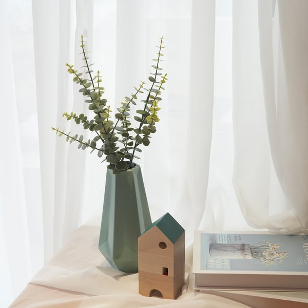 Minimalist decor: green vase with eucalyptus, wooden house, sheer curtains.