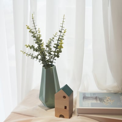 Minimalist decor: green vase with eucalyptus, wooden house, sheer curtains.