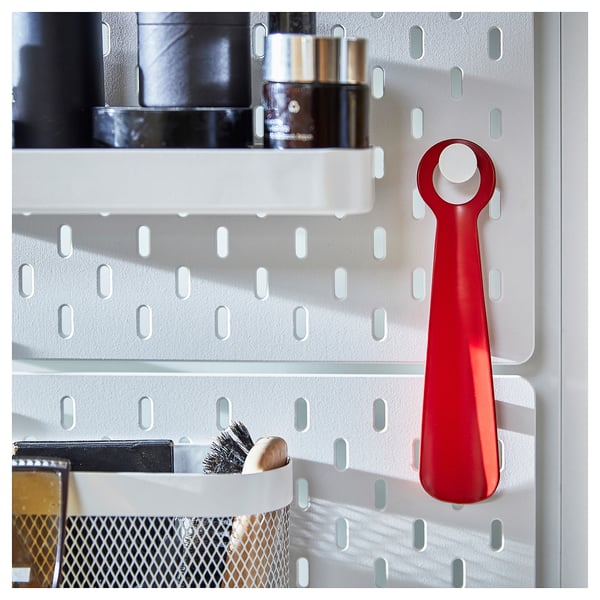 Bright red SNÖSKYFFEL shoehorn hangs on wall panel, small, metal.