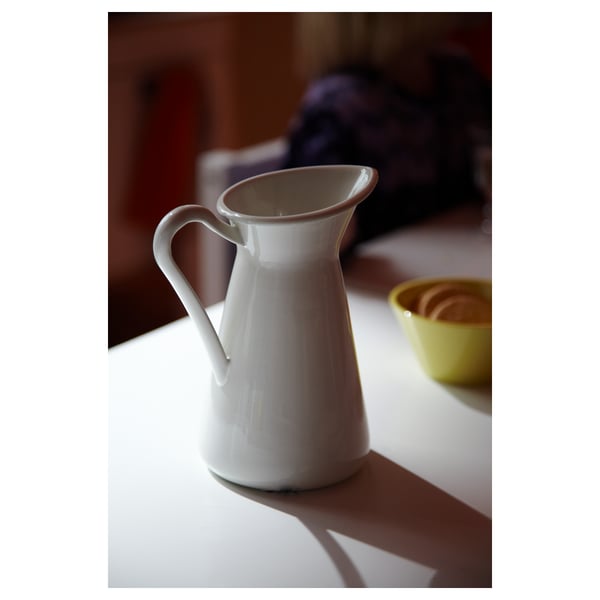 A white SOCKERÄRT enamel pitcher. It has a handle and a spout, and is placed on a white surface.