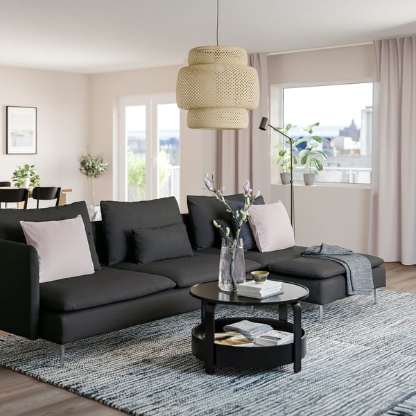 Modern black SÖDERHAMN sofa with high legs and deep seats. Large section with pillows, below a hanging yellow lamp.