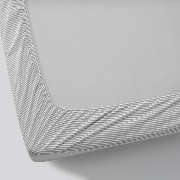A close-up of a neatly made bed with a light grey striped fitted sheet; shows quality and fit.