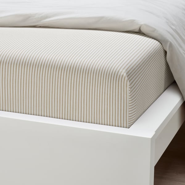 A neatly made bed with a striped beige and white fitted sheet on a white bed frame. The sheet appears soft and well-tucked, suggesting high quality.