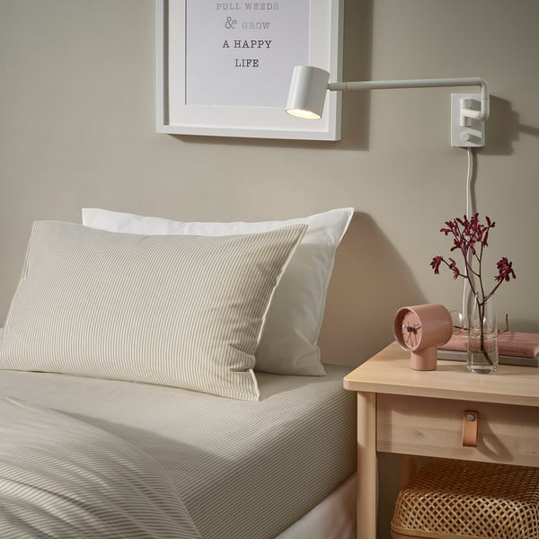 Cosy bedroom with grey SOLFIBBLA pillow on bed, beige wall light, and small flowers.