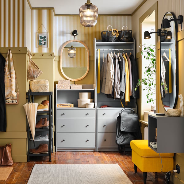 Modern entryway with striped walls, grey cabinets, coats, SOLKLINT lamps, yellow bench, and umbrella stand.