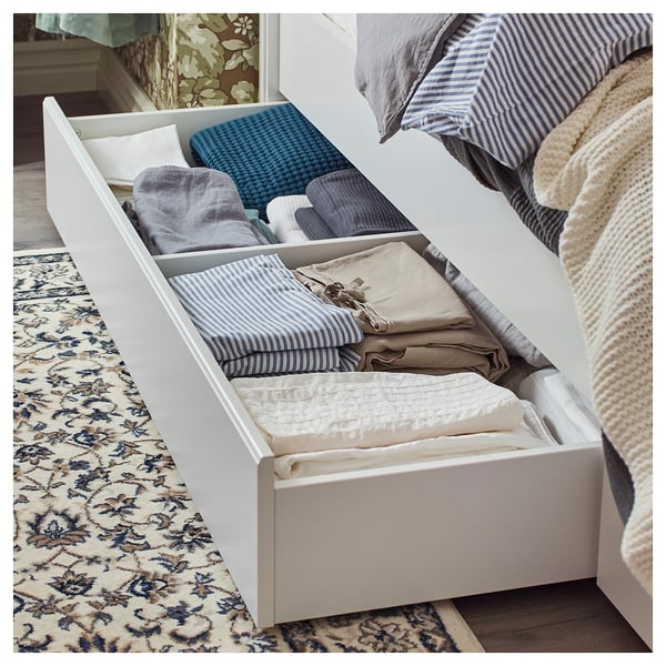 Open white under-bed storage drawer, neatly folded striped and solid bed linens inside.