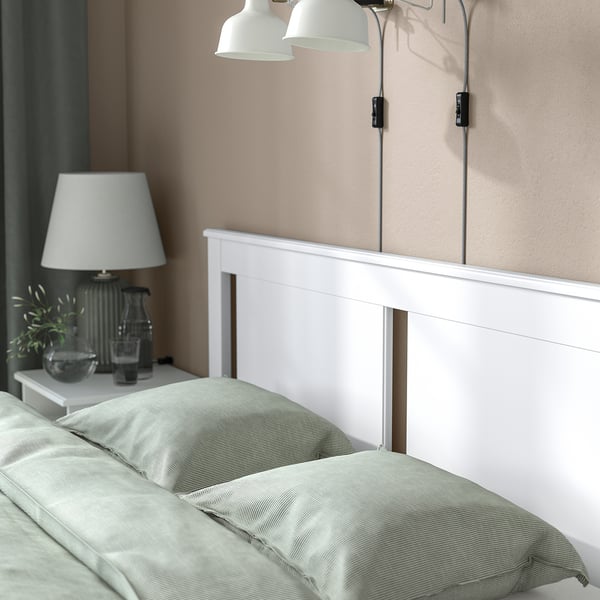 Minimalist bed with soft edges, high legs, and under-bed storage. Two wall lamps are mounted above it.