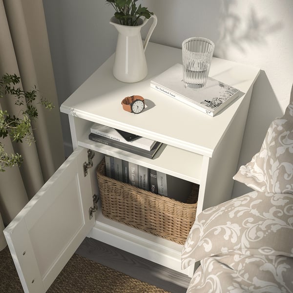 White bedside table with adjustable door opening, hidden cable outlet, storing books in basket and tabletop items.