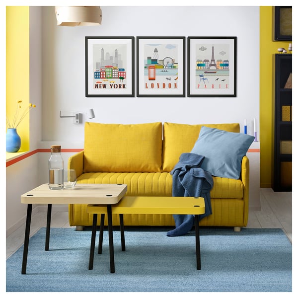 Bright living room with yellow sofa, blue pillows, nesting tables, city posters, and blue rug.