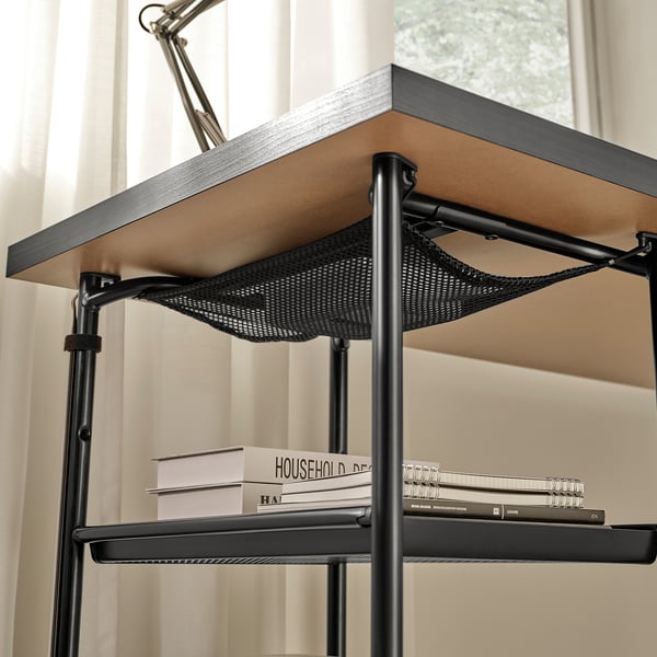 Black metal desk with adjustable shelf holding books and notepads, featuring cable management under the shelf.