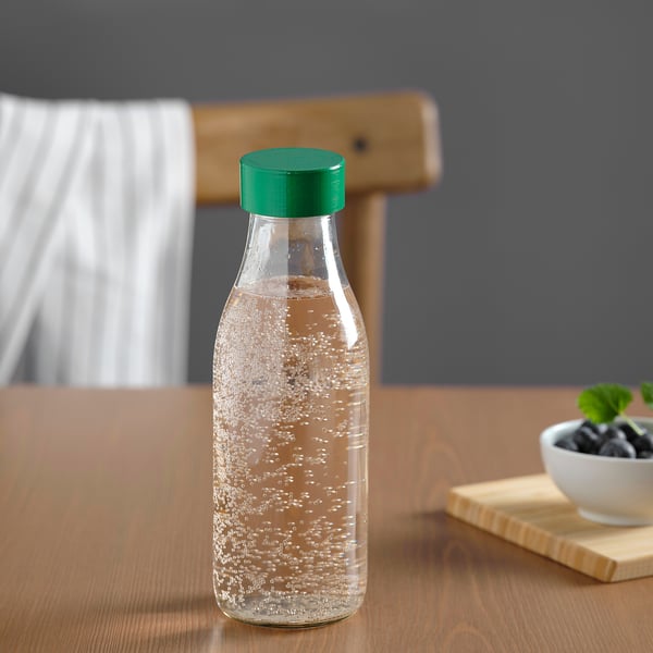 Clear glass water bottle with green cap on wooden table.