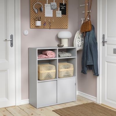 Modern grey storage cabinet with open shelves, closed cabinets, and a lamp. Pegboard and coat rack nearby for additional storage.