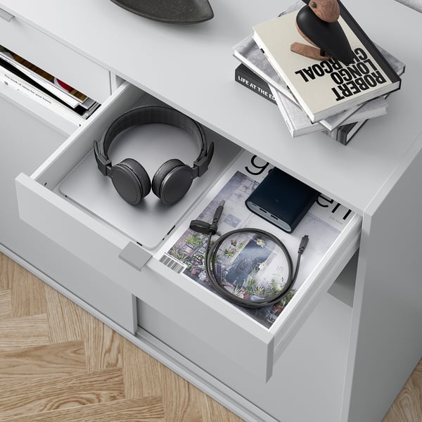 White desk drawer open, displaying black headphones, power bank, and coiled cable on a magazine.