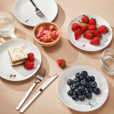 Assorted fruits and cake on varied plates with fun designs. Includes forks and knife.
