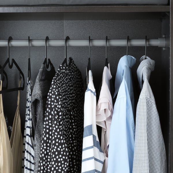 Closet with black hangers holding shirts and patterned clothes, saving space efficiently.