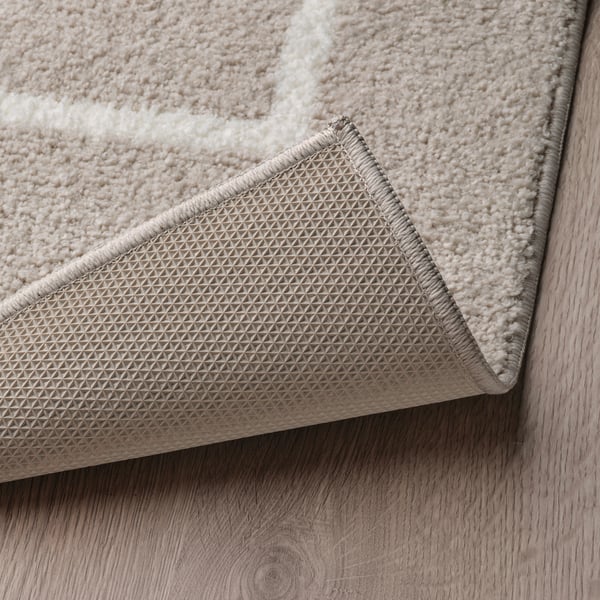 Close-up of a plush, beige rug with textured, non-slip backing on a wooden floor.