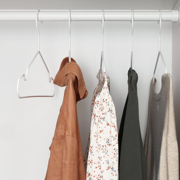 Four clothes hangers with various garments hang neatly in a row, efficiently using wardrobe space. The hangers feature grooves to prevent sliding.
