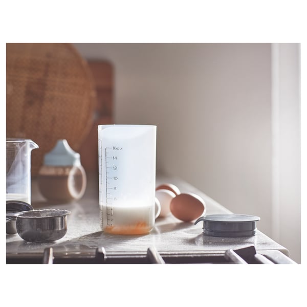 White shaker with leak-proof lid on kitchen counter, marked for measurements, mixed liquid, baking tools.