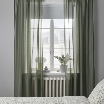 Two green STENFRÖ sheer curtains hang straight, offering a sense of calm. Made from recycled polyester, they diffuse sunlight, adding privacy.