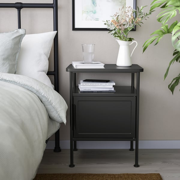Black STJÄRNÖ bed with high headboard, matching bedside table holding books, glass, and flowers, white pillows, and striped bedding.