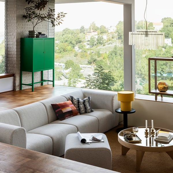 Modern living room STOCKHOLM 2025 sofa in neutral fabric, large windows, green cabinet, wooden floor. Cosy, spacious, with natural light.