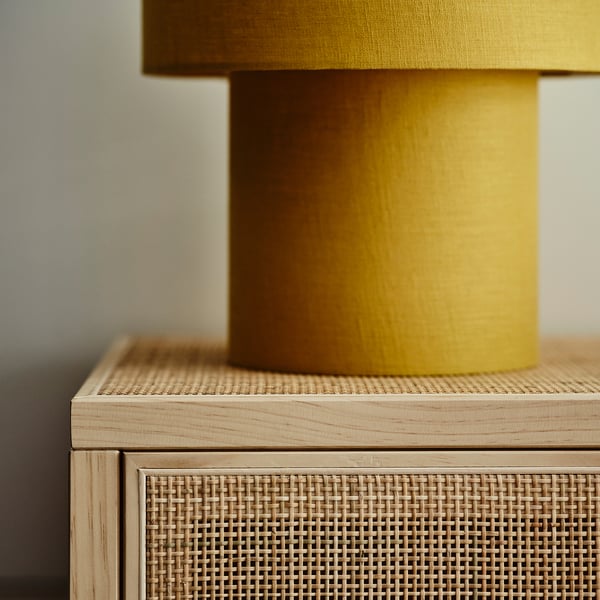 Yellow lamp with wooden base on woven rattan cabinet.
