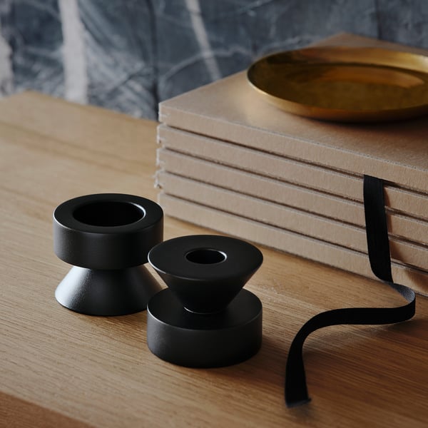 Two black metal candlesticks on wooden table, one side for tall candles, one for tealights, next to stacked books and gold dish.