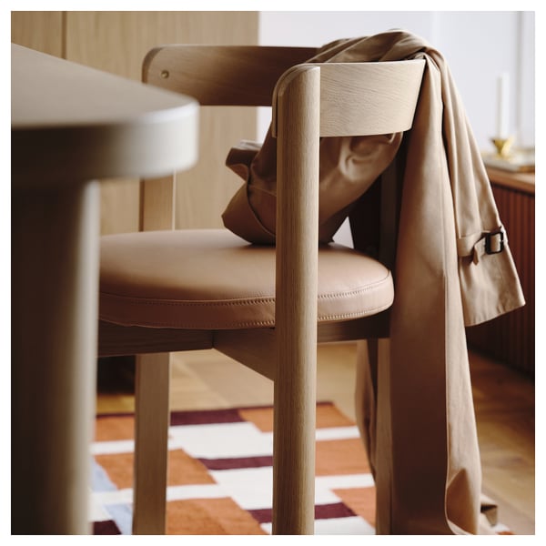 Light-colored wooden chair with beige leather seat, back, and jacket draped over the back. Showcasing modern scandinavian design and comfort.