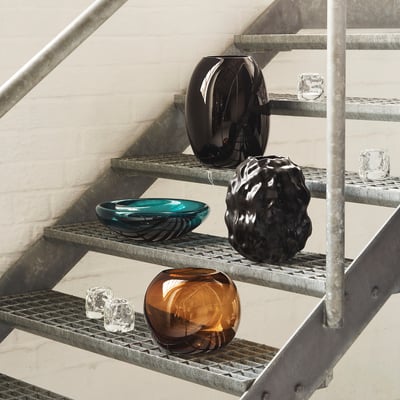 Modern glass vases in dark colours on steel steps. Includes brown, black, and teal pieces, with glass cubes adding to minimalist, industrial look.
