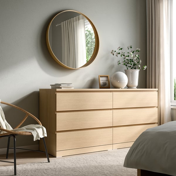 Modern bedroom with large gold STOCKHOLM mirror, oak dresser, and minimalist decor.