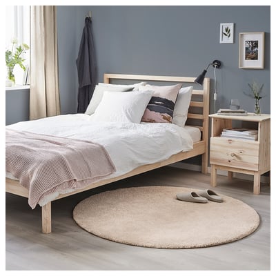 A cozy bedroom with a beige round STOENSE rug, a light wood bed with white linens, and a light wood nightstand.